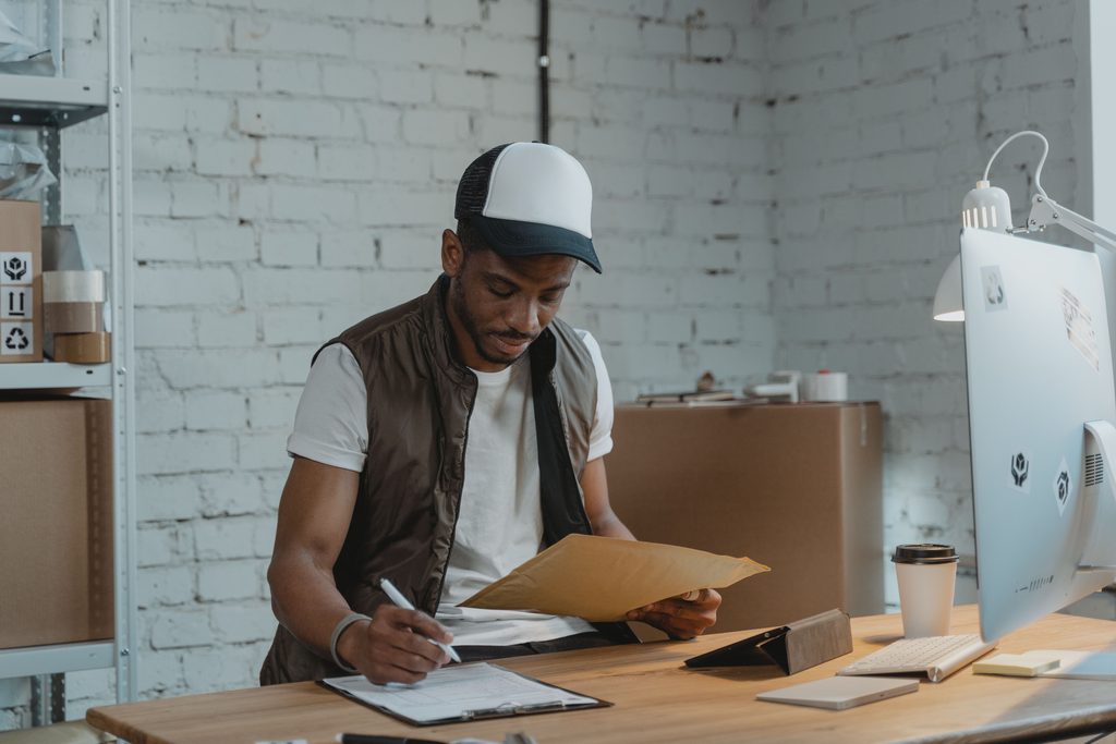 A logistics professional writing on a clipboard in front of a computer